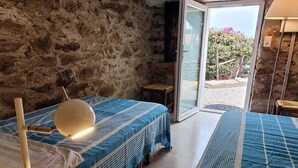 Una habitación con dos camas, una mesita de noche de madera, una lámpara y una pared de piedra.
