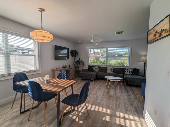 Un salon moderne comprenant un coin repas, de grandes fenêtres, un ventilateur de plafond et un téléviseur à écran plat.