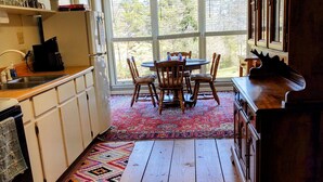 A kitchen with wooden floors, a dining table with chairs, a window with blinds, and a kitchen counter with a coffee maker. - Charming 1892 Log Cabin in the Blue Ridge Mountains foothills (Rutherfordton)