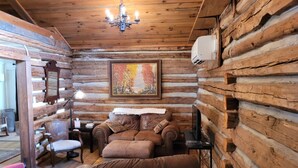 A log cabin interior with a leather sofa, a pink chair, a painting, and a chandelier. - Charming 1892 Log Cabin in the Blue Ridge Mountains foothills (Rutherfordton)