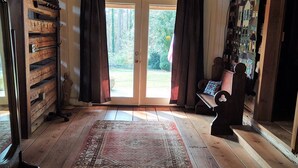 A spacious room with wooden floors, a large rug, a bench, and a view through a glass door. - Charming 1892 Log Cabin in the Blue Ridge Mountains foothills (Rutherfordton)