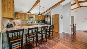 A spacious kitchen with wooden cabinets, a large island with bar stools, and a skylight. - Outdoor Pool ● Near Boone & Elk ● Fire Pit ● Games ● Kids Bunks (Banner Elk)