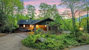 A rustic cabin with a stone exterior, a wooden deck, and a garden area. - Outdoor Pool ● Near Boone & Elk ● Fire Pit ● Games ● Kids Bunks (Banner Elk)