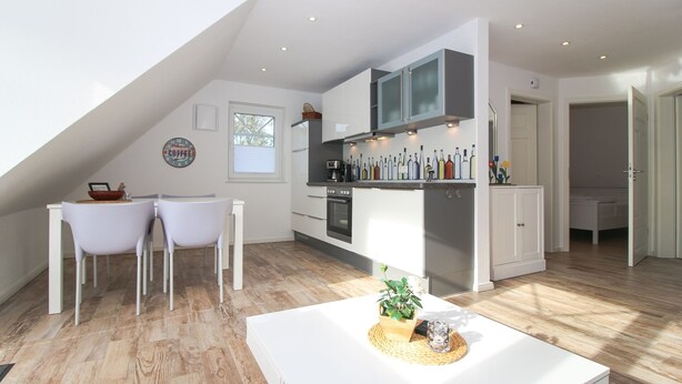 A modern kitchen with white cabinets, a dining area with two chairs, and a wooden floor.