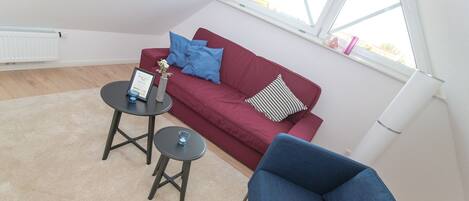 Una sala moderna con un sofá rojo, dos mesitas y un sillón azul.