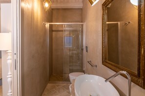 A bathroom with a glass-enclosed shower, a white sink, and a large mirror with a gold frame.