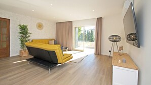 A modern living room with a sofa, a TV, and a sliding glass door leading to an outdoor area. - Villa w/ heatable pool, BBQ & private annexes (Albufeira)