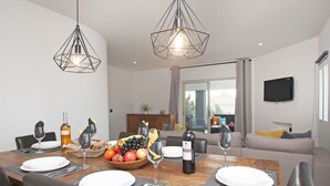 A dining area with a wooden table set for four, surrounded by leather chairs. There are two pendant lights, a television mounted on the wall, and a sofa in the background. - Villa w/ heatable pool, BBQ & private annexes (Albufeira)