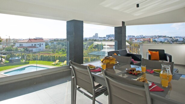 A balcony with a dining table set for breakfast, a swimming pool, and a city view. - Villa w/ heatable pool, BBQ & private annexes (Albufeira)