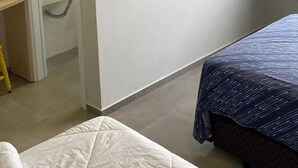 Una habitación con cama, televisión instalada en la pared y baño visible a través de una puerta abierta.