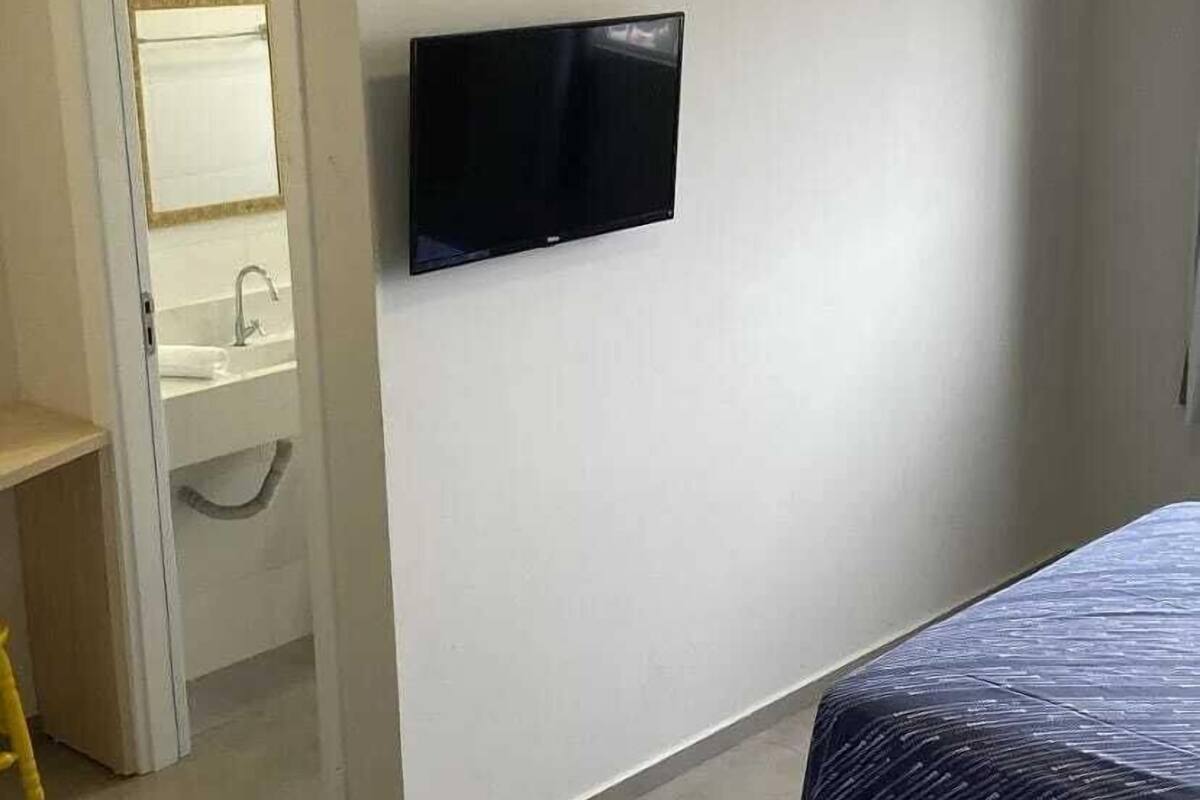 Une chambre avec un lit, un téléviseur fixé au mur et une salle de bain visible à travers une porte ouverte.