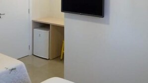 Una habitación de hotel con cama, escritorio, televisor montado en la pared y un refrigerador pequeño.