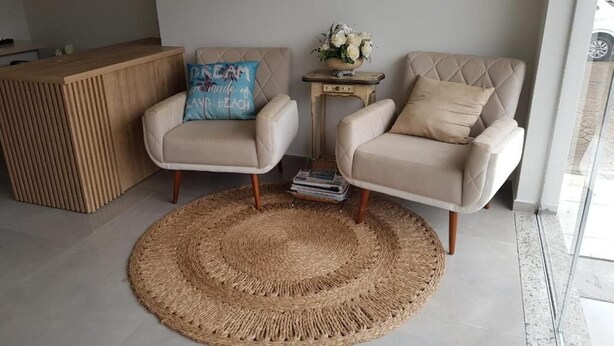 Una sala moderna con dos sillones color beige, un mostrador de recepción de madera y una alfombra tejida.
