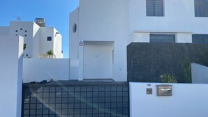 Edifici modern amb façana blanca, entrada tancada amb reixa i mur de pedra.