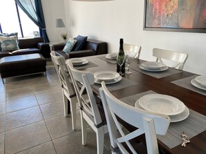 Un comedor con una mesa dispuesta para cuatro personas, sillas blancas y una botella de vino sobre la mesa.