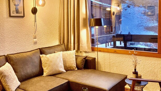 A modern living room with a sectional sofa, a round coffee table, and a view of a snowy landscape through a large window. - Spacious and clean appart. (4-6 pers.) on piste at Altispace, very centrally located (Valmorel)