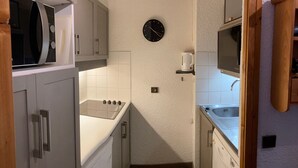 A compact kitchen with white cabinets, a stove, a sink, and a clock on the wall. - Spacious and clean appart. (4-6 pers.) on piste at Altispace, very centrally located (Valmorel)