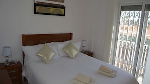 A neatly made bed with white linens and two gold pillows, a bedside lamp, and a folded towel on the floor. - 2 bed ground floor Puerto marina (Los Alcázares)