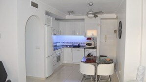 A compact kitchen with white cabinets, a microwave, a toaster, and a glass dining table with two chairs. - 2 bed ground floor Puerto marina (Los Alcázares)