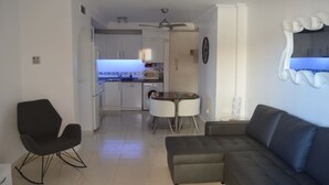 A modern living room with a sofa, a dining table with chairs, and a kitchen in the background. - 2 bed ground floor Puerto marina (Los Alcázares)