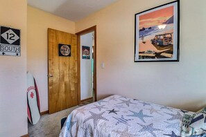 Un dormitorio con cama, una puerta con un letrero que dice 'Zona sin interrupciones', una tabla de surf y un cuadro enmarcado de una playa.