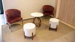 Een kamer met twee rode fluweelarmstoelen en een witte tafeltje met een rond poef.