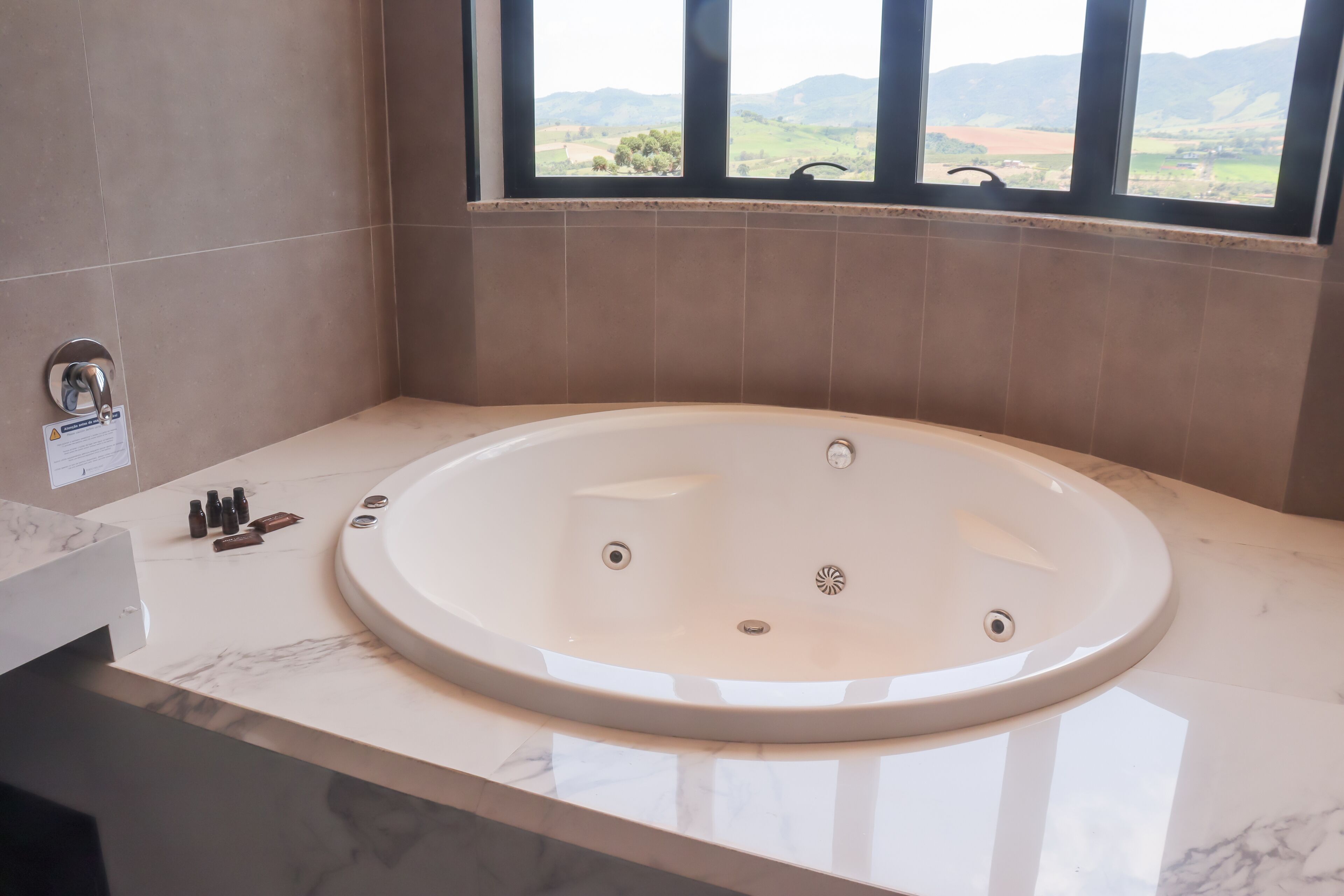 A modern bathroom with a large bathtub, a vanity with a marble countertop, and a window offering a view of the countryside.