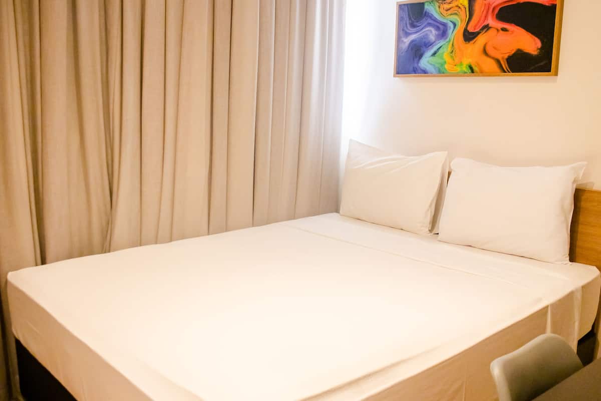 A neatly made bed with white linens, a wooden headboard, and a single chair.