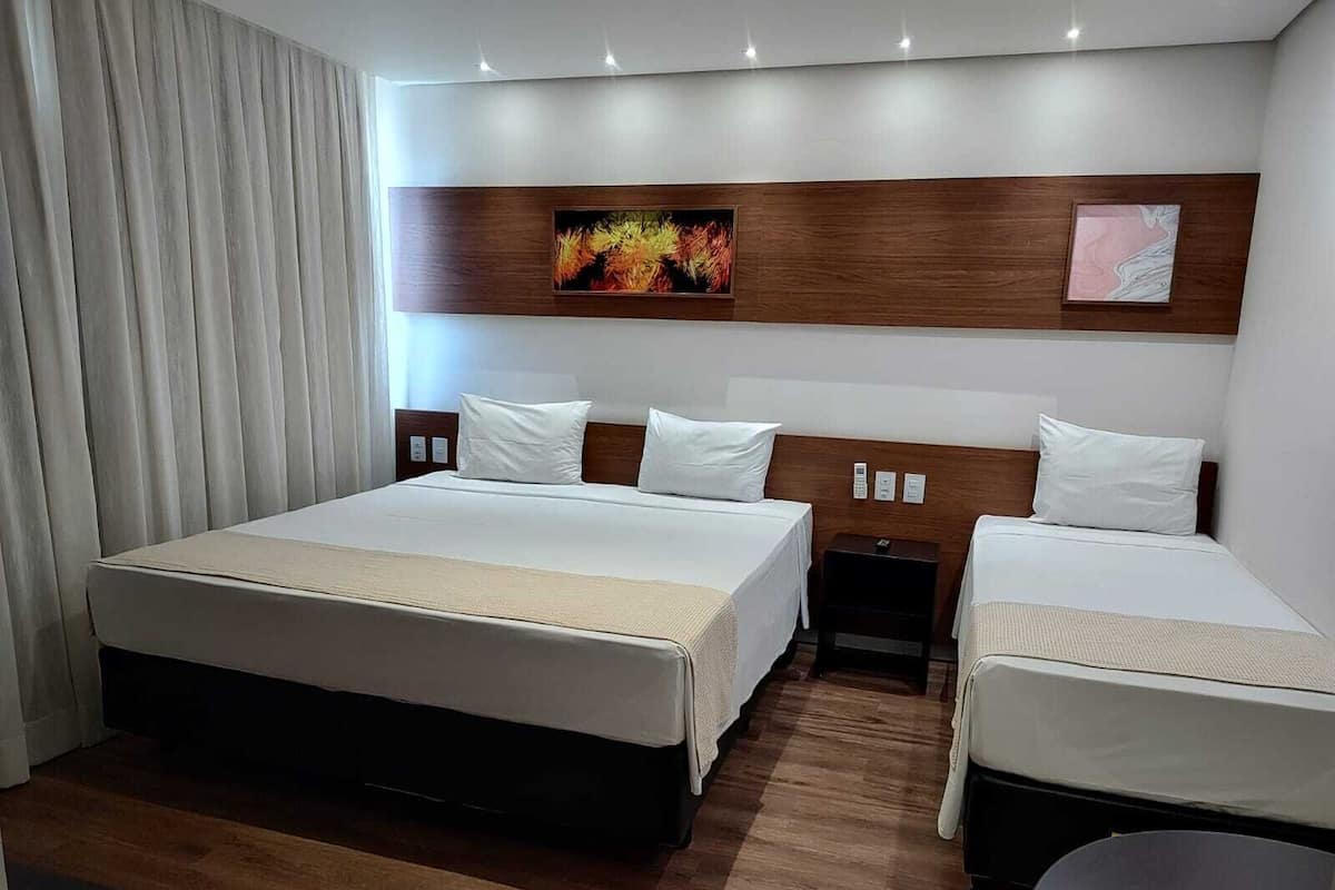 A hotel room with a large bed, two bedside tables, a small table, and a wall-mounted artwork.