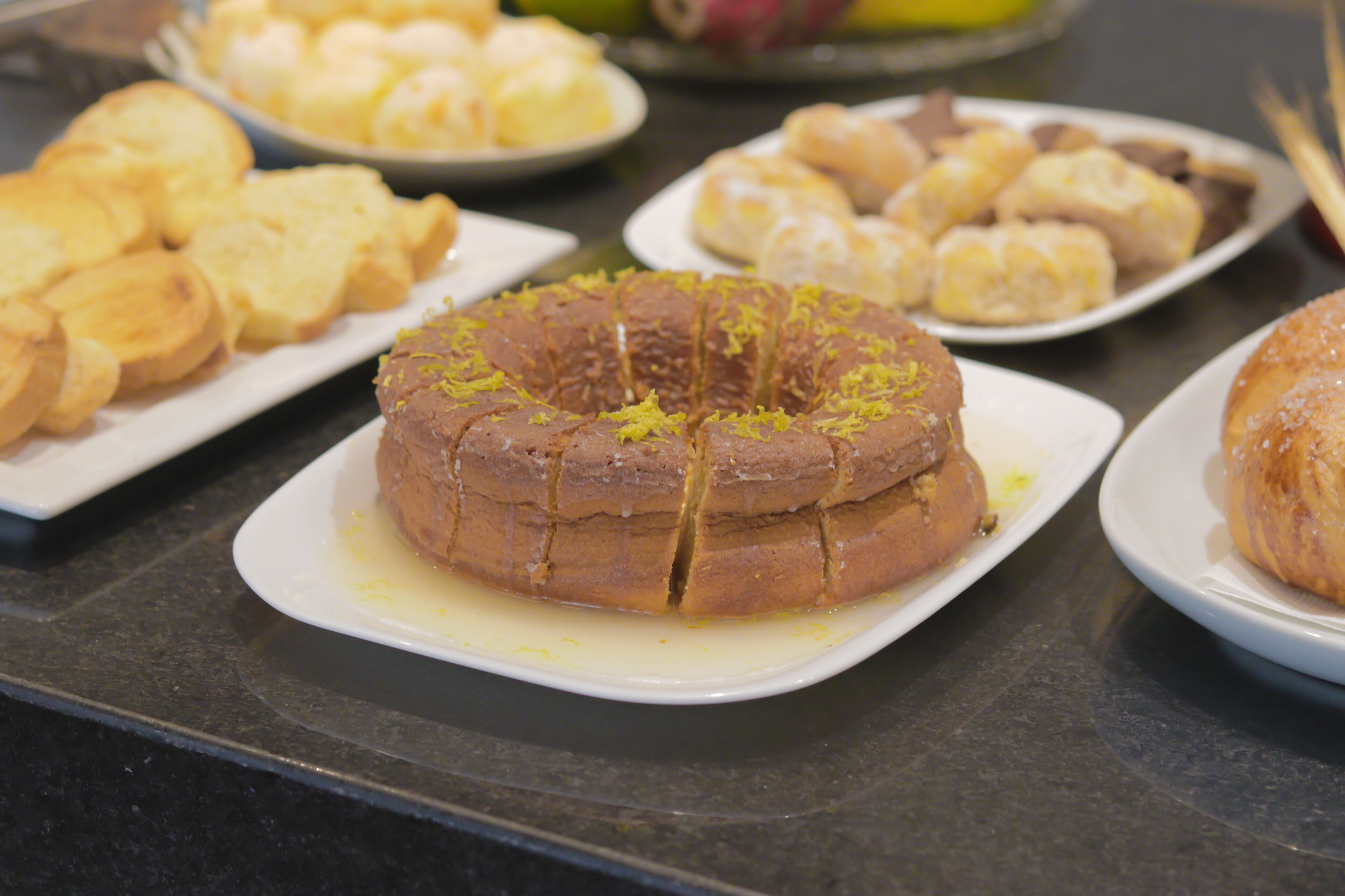 A variety of baked goods on a counter, including a cake with yellow zest on top.