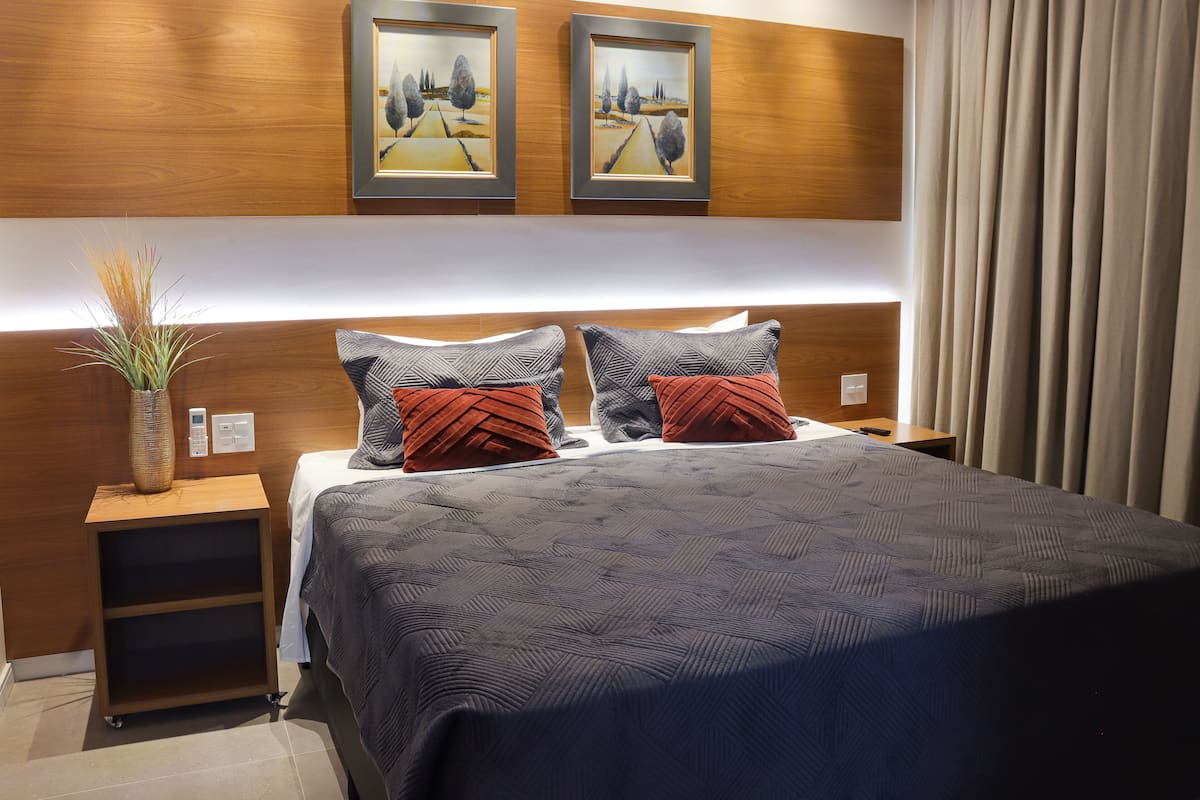 A modern hotel room with a large bed, two nightstands, a wooden headboard, and two framed landscape paintings.