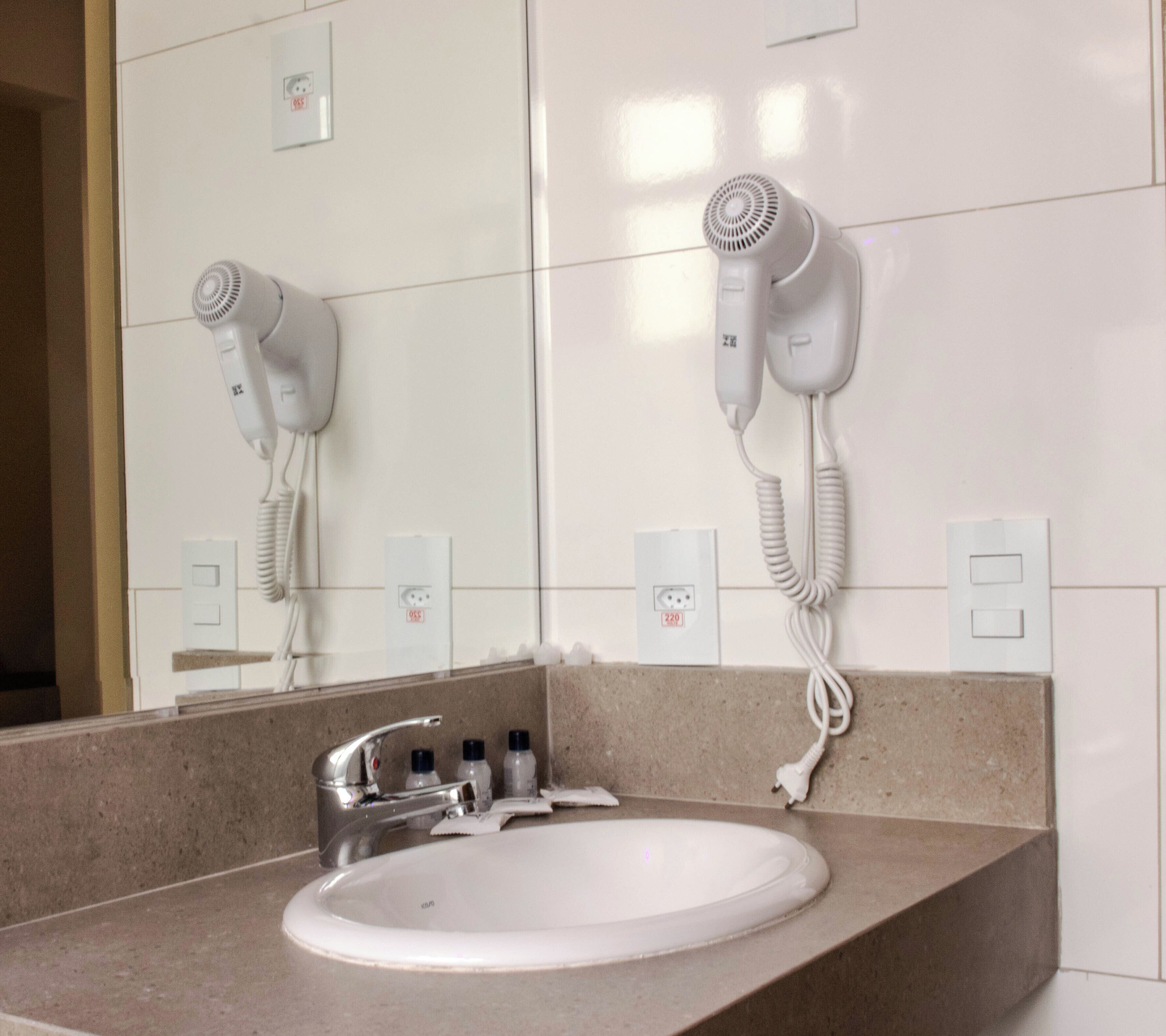 A bathroom with a sink, mirror, and two hair dryers mounted on the wall.