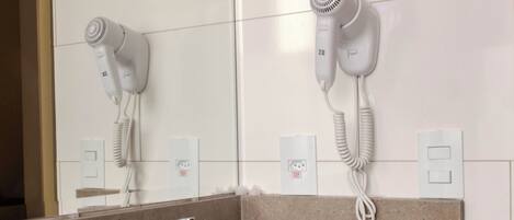 A bathroom with a sink, mirror, and two hair dryers mounted on the wall.