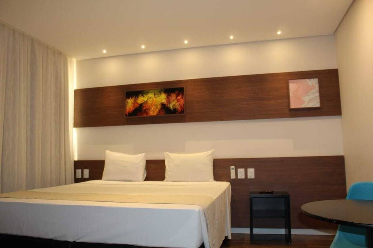 A hotel room with a large bed, a small table, and a painting on the wall.