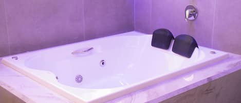 Un baño moderno con una bañera grande, un cabezal de ducha manual y un asiento integrado.