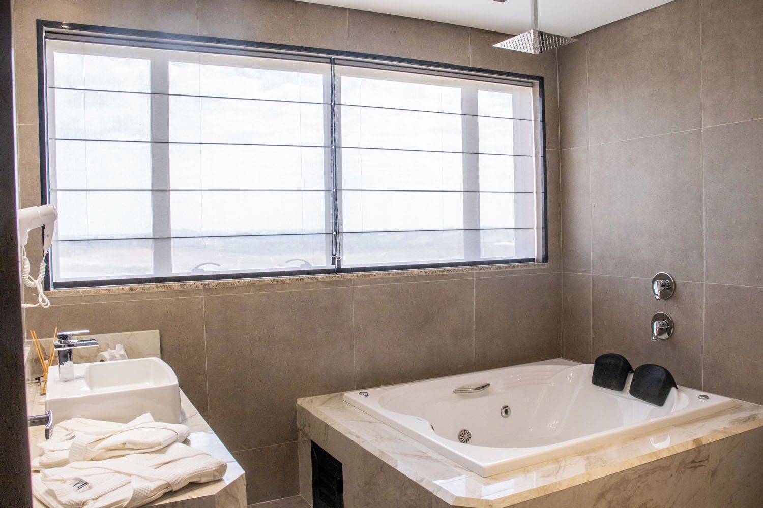A modern bathroom with a large window, a bathtub, and a vanity with towels.
