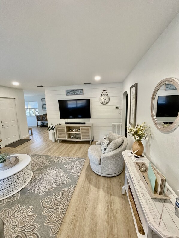 A modern living room with a flat-screen TV, a round coffee table, a grey armchair, and a decorative mirror.
