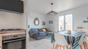 A modern kitchen with a gas stove, oven, and a dining area with a table and chairs. - La Marine - Jardin - Golf (Pornic)