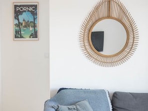 Una habitación con un espejo redondo con marco de bambú, un cuadro en la pared y un sofá con cojines estampados.