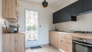 A modern kitchen with wooden cabinets, a built-in oven, and a coffee maker. - La Marine - Jardin - Golf (Pornic)