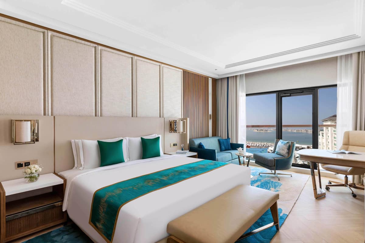 A hotel room with a large bed, a desk, a chair, and a view of the city.