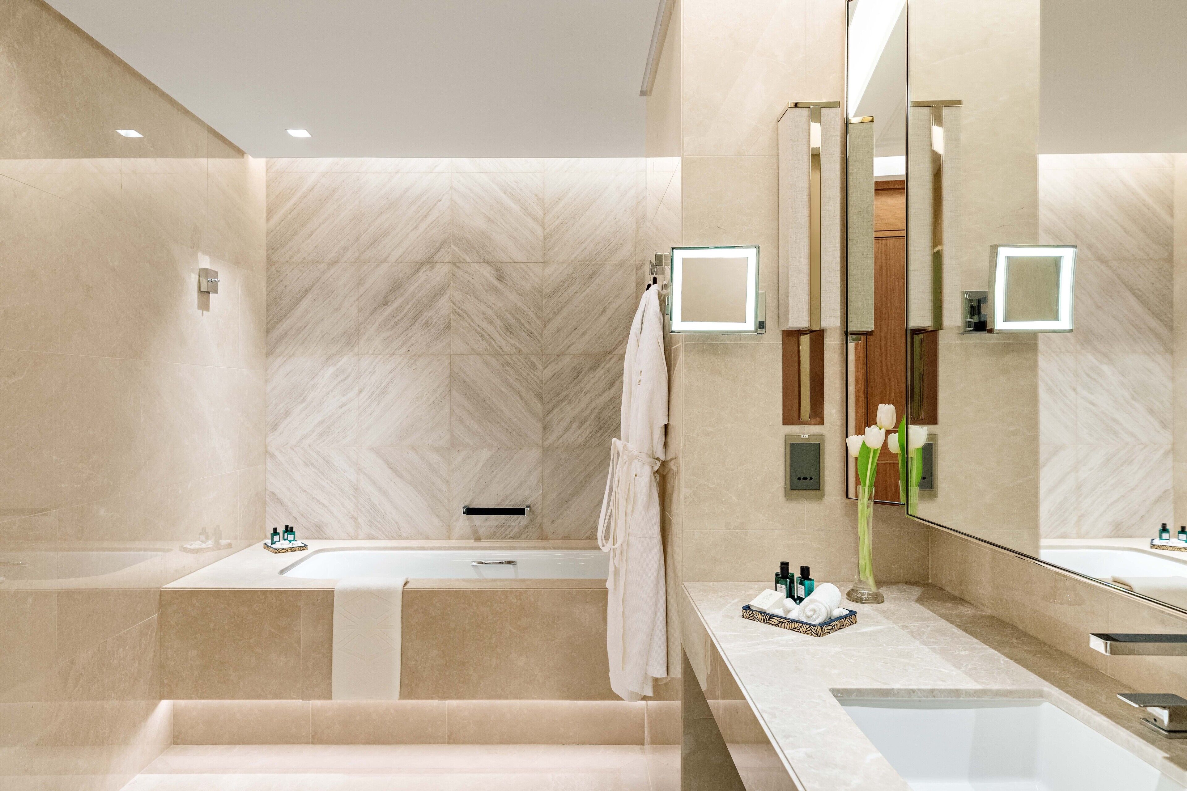 A modern bathroom with a large mirror, two sinks, and a bathtub.