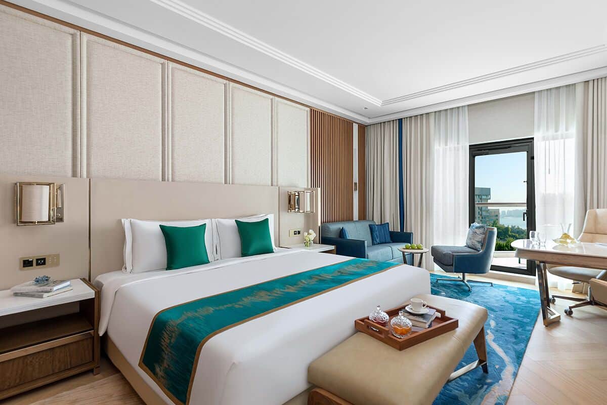 A hotel room with a large bed, a desk, a chair, and a view of the city.