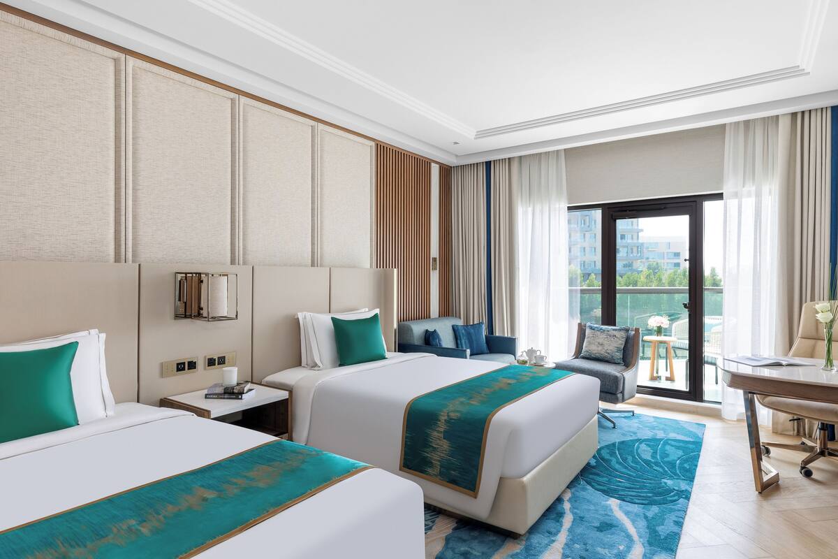 A hotel room with two beds, a desk, and a balcony with a view.