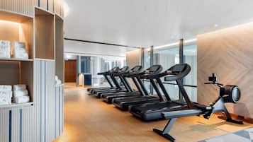 A gym with multiple treadmills lined up against a wall with a wooden finish and a shelf with towels.