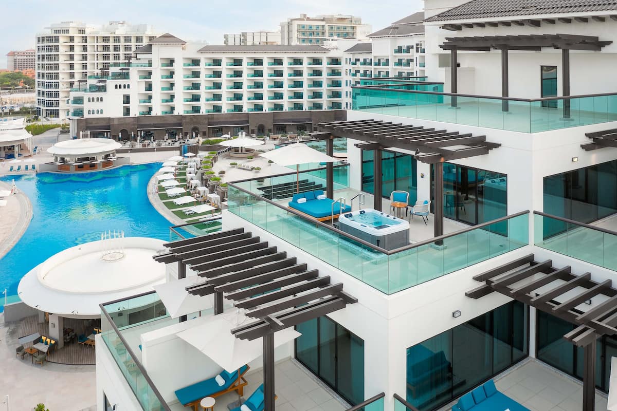 A modern hotel with a rooftop pool area, glass railings, and multiple lounge areas.