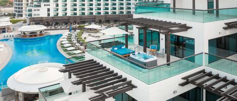 A modern hotel with a rooftop pool area, glass railings, and multiple lounge areas.