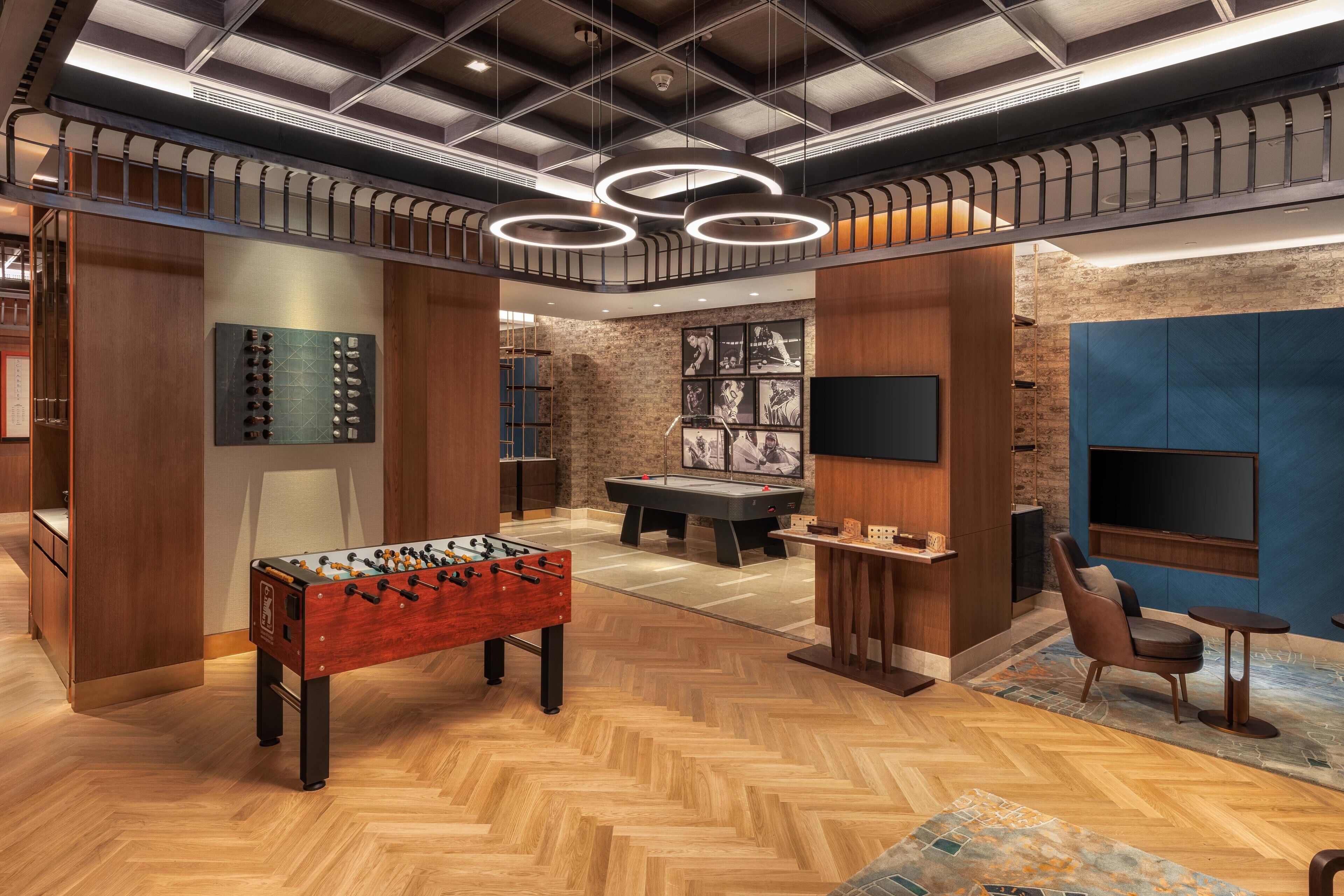 A modern indoor space with a foosball table, a pool table, and a seating area with a TV.