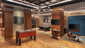 A modern indoor space with a foosball table, a pool table, and a seating area with a TV.