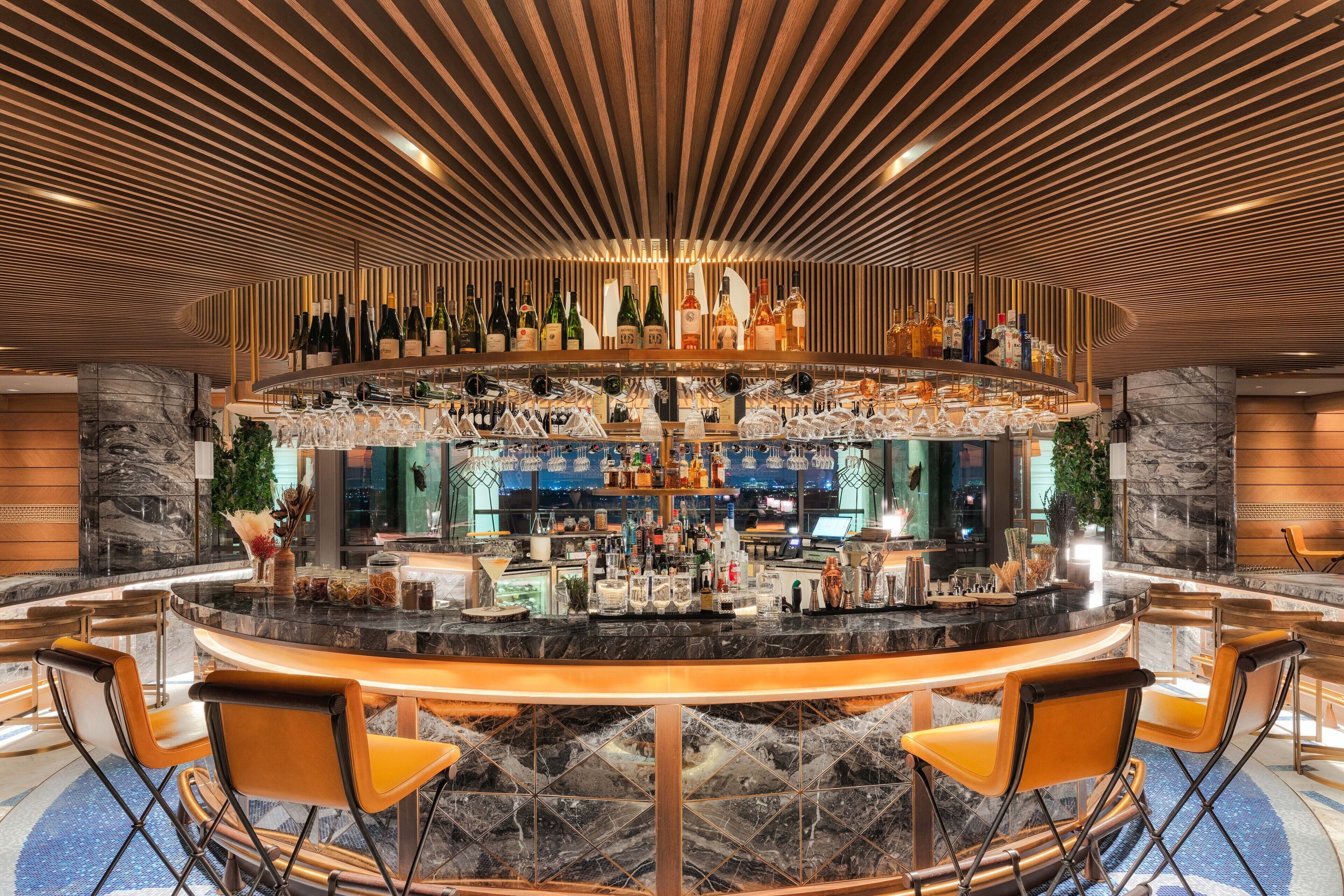 A bar area with a curved marble countertop, multiple bar stools, and a variety of bottles and glasses.